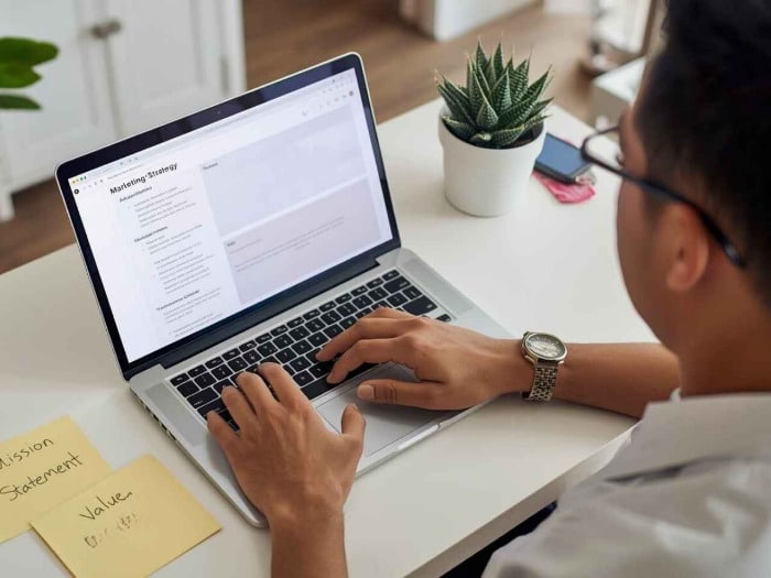 a person types on a laptop displaying a marketing strategy document. beside them, sticky notes read mission statement and value. a small potted plant adds greenery.
