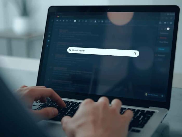 a person types on a laptop with a dark-themed interface, displaying a search bar in focus. calm, focused atmosphere, highlighting tech and productivity.