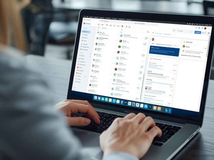 hands typing on a laptop displaying a complex email interface, with a sidebar of contacts and open messages, evoking a sense of productivity